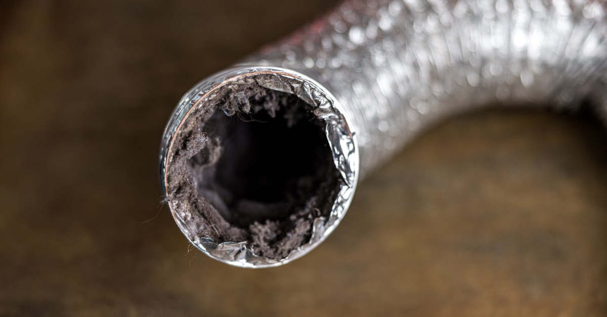 An aluminum dryer vent hose sitting on the ground while the end is open with a large visible dust buildup.