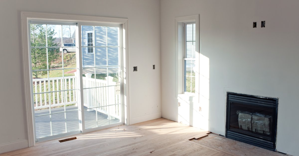 In an unfinished room, there are windows letting in some light and a small fireplace with a glass door.