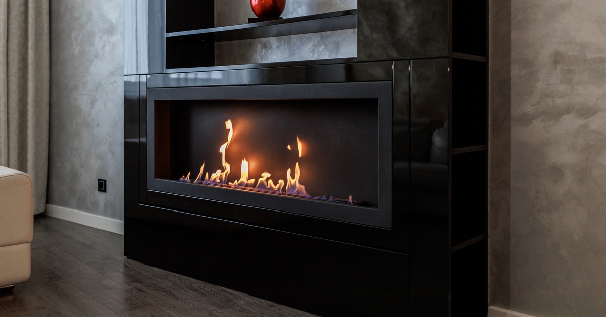 A gas fireplace built into a bookshelf. The shelving unit is black and has a bright red cherry on one of the shelves.